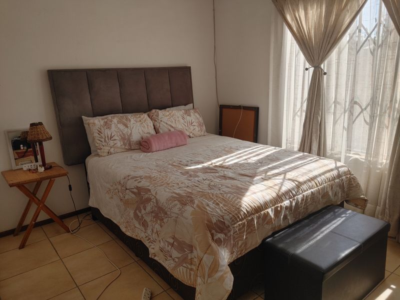 A bedroom featuring tiled flooring and a window fitted with a security gate and curtain rails, receiving natural light.