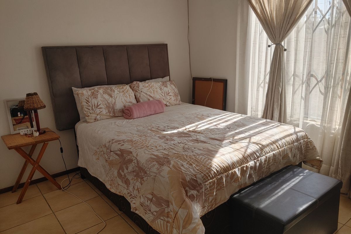 A bedroom featuring tiled flooring and a window fitted with a security gate and curtain rails, receiving natural light.