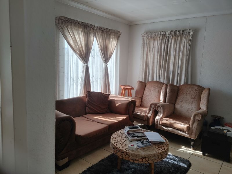A cozy living room featuring tiled flooring and natural light through large windows with installed curtain rails.