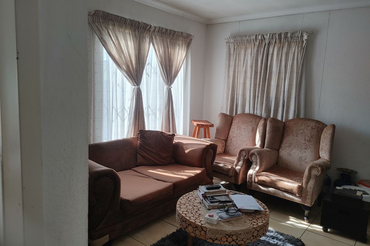 A cozy living room featuring tiled flooring and natural light through large windows with installed curtain rails.