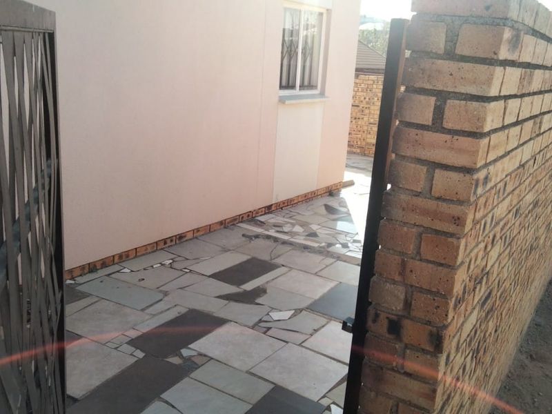 A view of the property entrance featuring a brick boundary wall, a security gate, and a paved walkway leading to the side of the building.