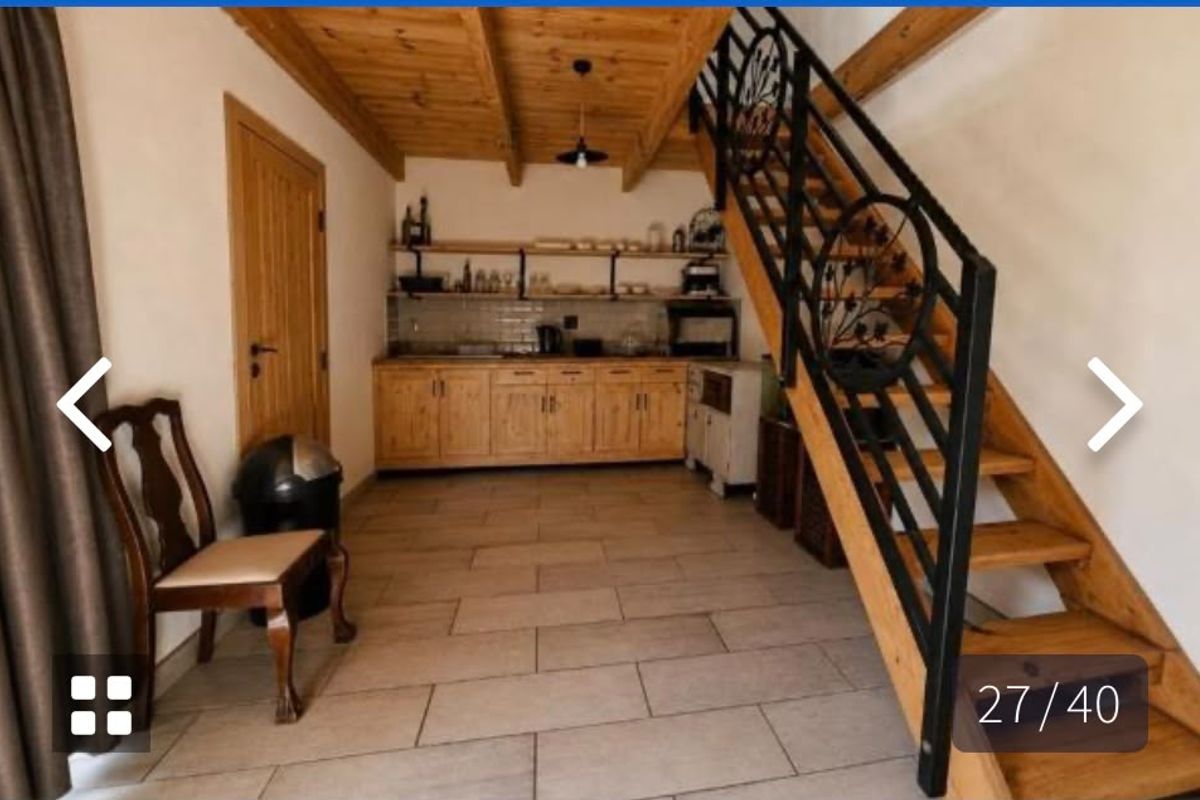 A rustic kitchen area featuring wooden cabinetry, open shelving, and a prominent wooden staircase with a decorative wrought iron railing.