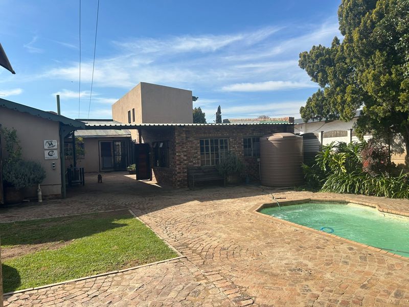 Rear exterior view featuring a swimming pool, paved courtyard area, covered patio, and a water storage tank set against a brick-walled structure.