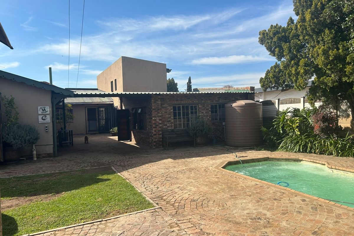 Rear exterior view featuring a swimming pool, paved courtyard area, covered patio, and a water storage tank set against a brick-walled structure.