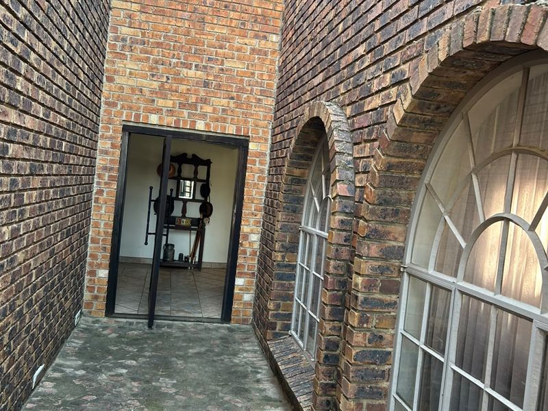 A narrow exterior walkway featuring exposed brick walls, arched windows, and stone paving leading to an interior entrance.