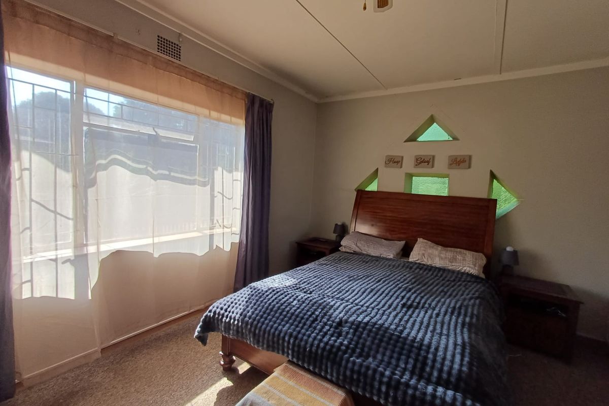 A bedroom featuring a large window with security bars, a ceiling fan, and unique decorative triangular windows above the bed area.