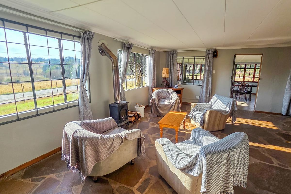 Spacious living room featuring rustic stone flooring, a cast iron fireplace, and large steel-framed windows with scenic rural views.