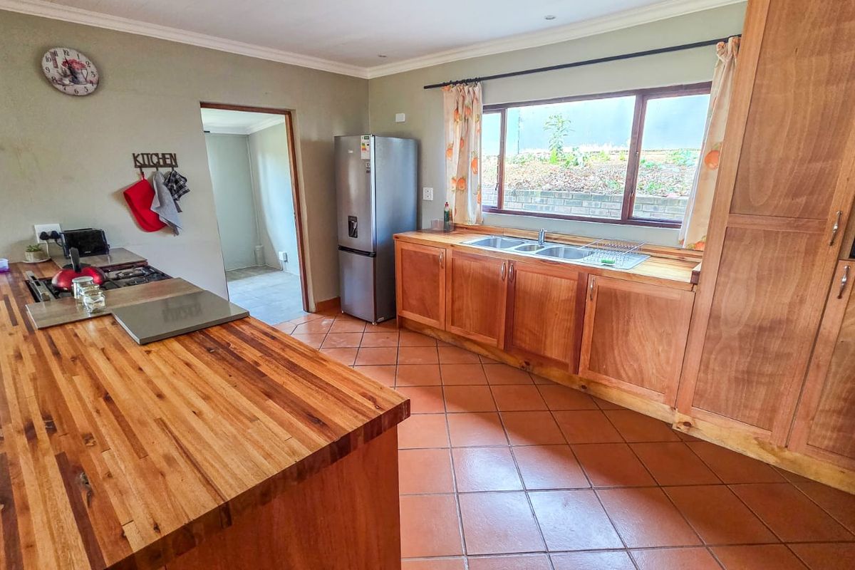 A functional kitchen featuring warm wooden cabinetry, butcher block countertops, a double basin sink, and terracotta floor tiles with a view to the garden.