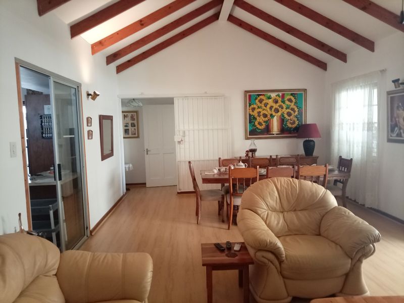 Open plan living and dining area featuring high vaulted ceilings with exposed timber beams and light laminate flooring.