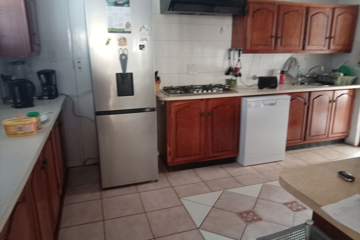 A functional kitchen featuring wooden cabinetry, a gas hob with extractor fan, tiled backsplash, and tiled flooring in a retirement village setting.