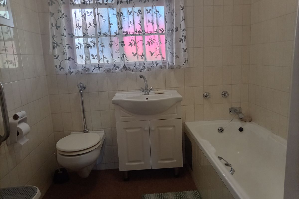 A functional bathroom featuring a wall-mounted toilet, vanity basin, and bathtub with full-height wall tiling.