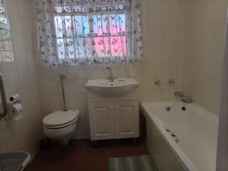 A functional bathroom featuring a wall-mounted toilet, vanity basin, and bathtub with full-height wall tiling.
