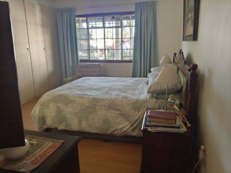 A comfortable bedroom featuring built-in cupboards, laminate flooring, and a window with security bars, offering a functional and well-lit living space.