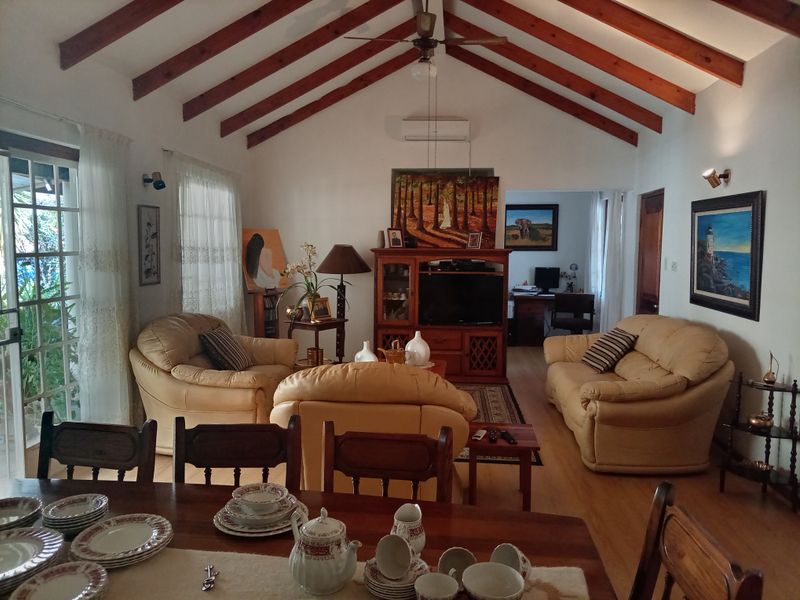 Spacious open-plan living and dining area featuring high vaulted ceilings with exposed timber beams, laminate flooring, and direct access to the patio.