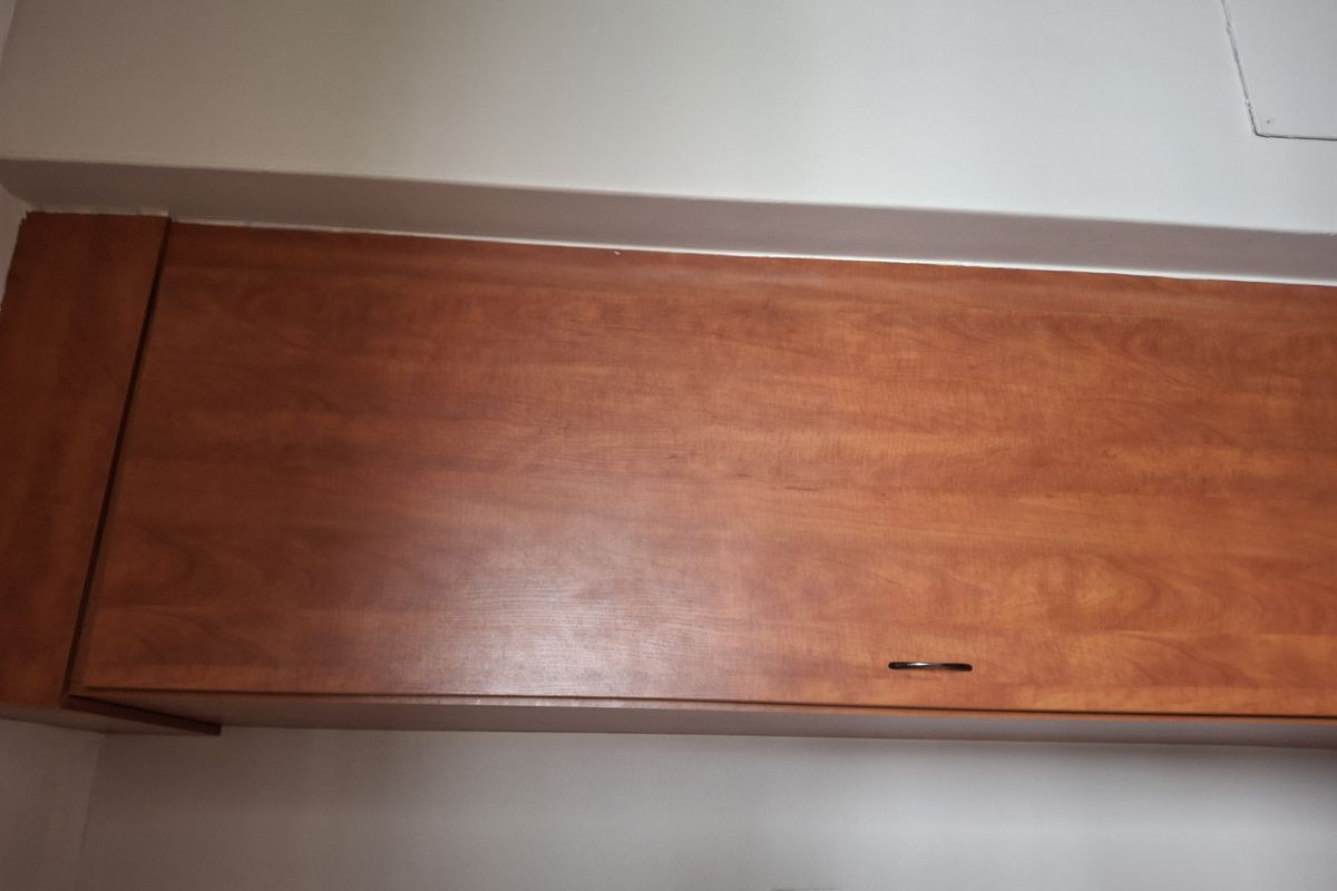 A simple bedroom featuring a single built-in wooden cupboard with a dark handle.