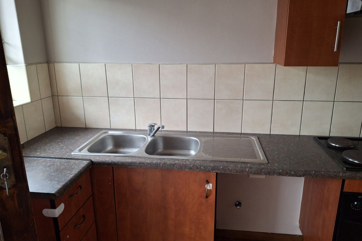 A functional kitchen area featuring a double bowl stainless steel sink, laminate countertops, tiled backsplash, and built-in wooden cabinetry with an integrated hob.