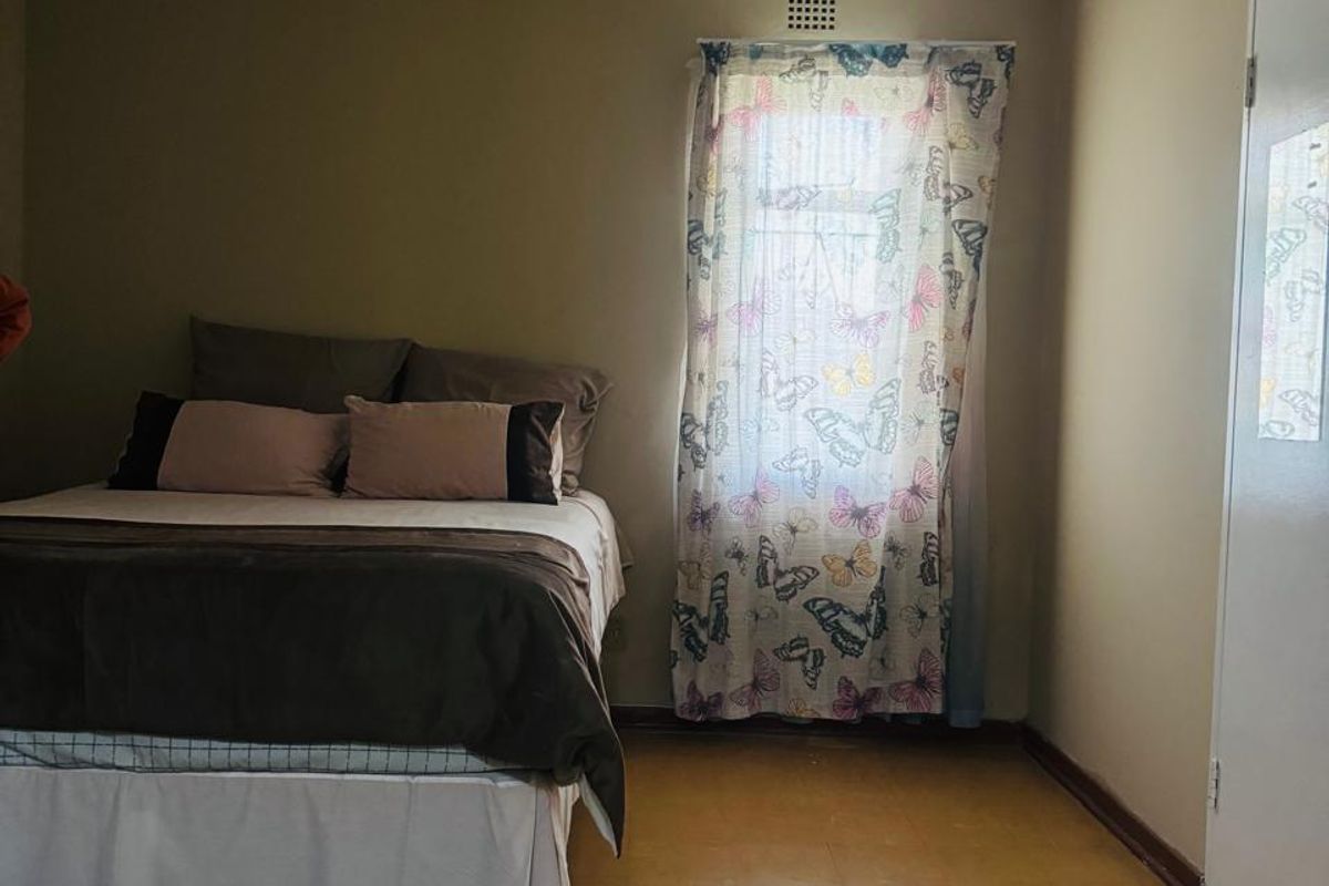 A simple bedroom featuring vinyl flooring and a ventilation brick, offering a functional space ready for cosmetic updates and modern finishes.