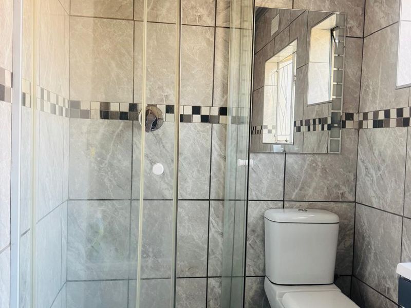 A modern bathroom featuring a walk-in shower with a rain shower head, glass enclosure, and contemporary tiled finishes throughout.
