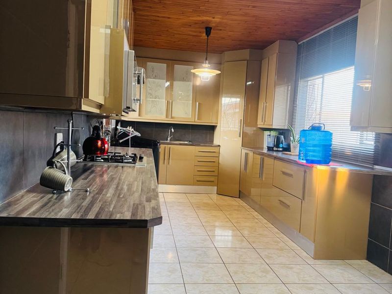 A functional kitchen featuring high-gloss cabinetry, laminate countertops, a gas hob, and a distinctive timber-paneled ceiling with tiled flooring throughout.