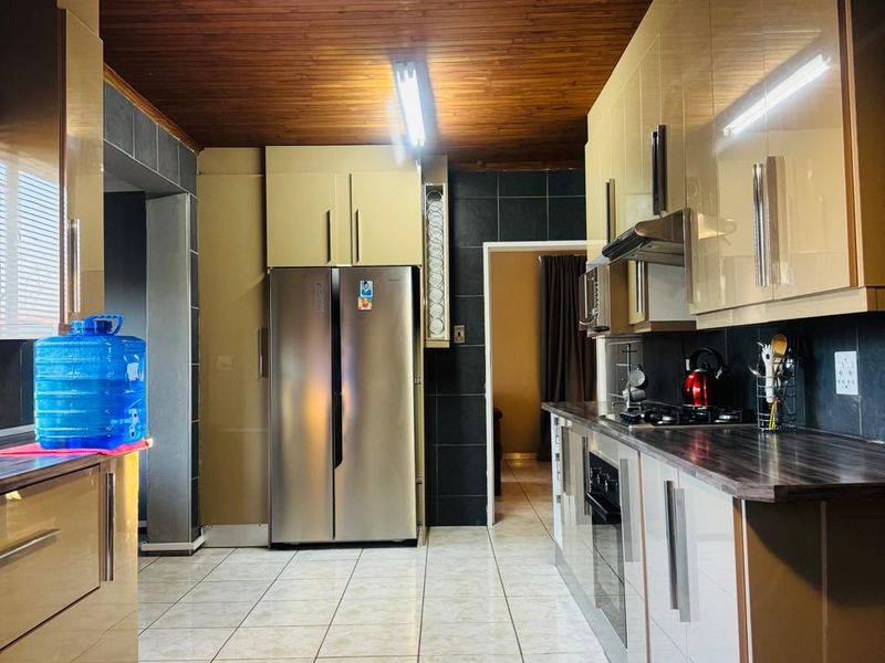 A functional kitchen featuring modern high-gloss cabinetry, dark laminate countertops, tiled flooring, and a distinctive timber-paneled ceiling.