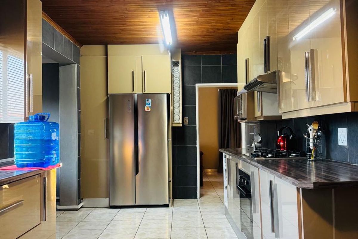 A functional kitchen featuring modern high-gloss cabinetry, dark laminate countertops, tiled flooring, and a distinctive timber-paneled ceiling.