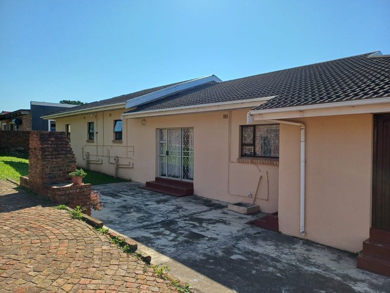 Rear exterior view of the house featuring a paved patio area, brick braai, and tiled roof with security gates on the sliding doors.