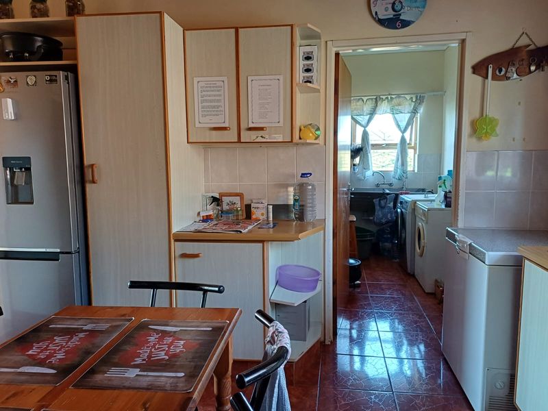 A functional kitchen area featuring built-in cabinetry and tiled flooring, with an adjacent scullery or laundry area visible through the doorway.