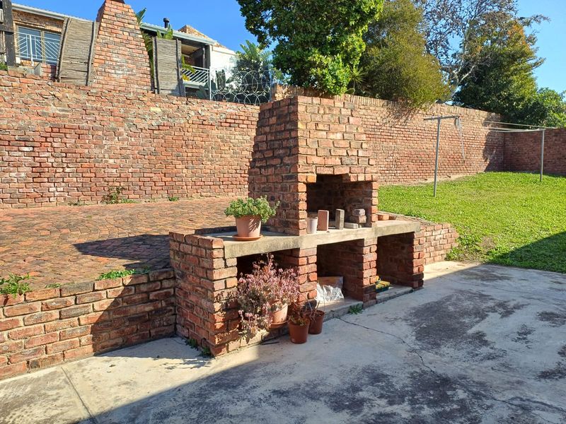 Rear garden area featuring a built-in brick braai, paved patio space, and a large brick retaining wall.