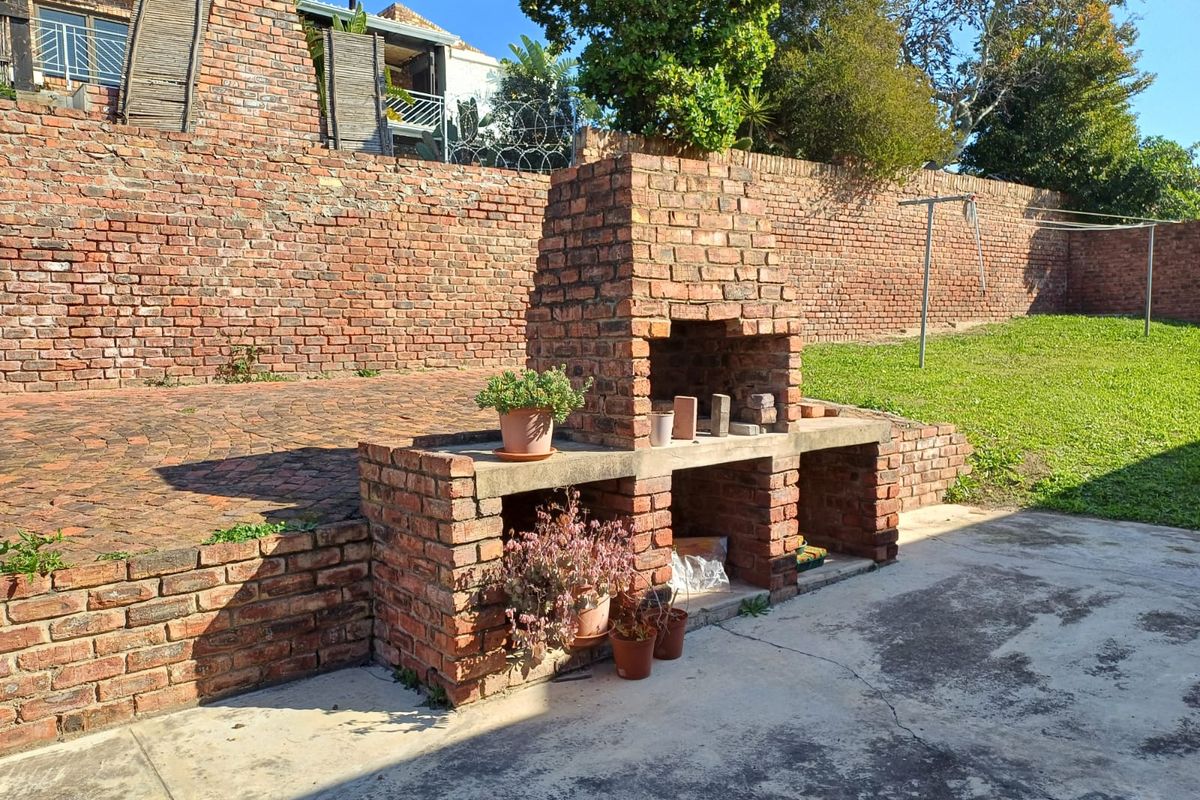 Rear garden area featuring a built-in brick braai, paved patio space, and a large brick retaining wall.