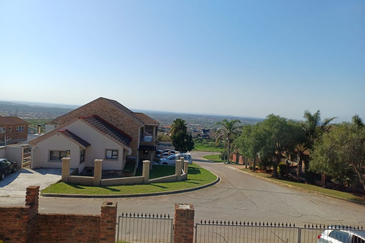 An elevated aerial view of the property showing the front facade, driveway, brick boundary walls, and surrounding neighborhood landscape.
