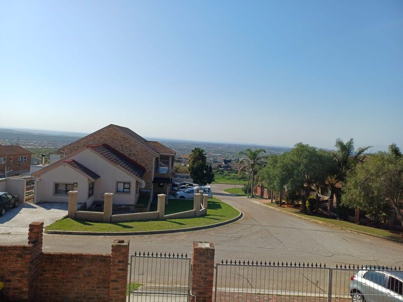 An elevated aerial view of the property showing the front facade, driveway, brick boundary walls, and surrounding neighborhood landscape.