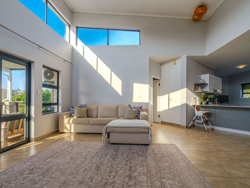 Spacious open-plan living area featuring high ceilings, clerestory windows for natural light, tiled flooring, and seamless access to an outdoor patio.
