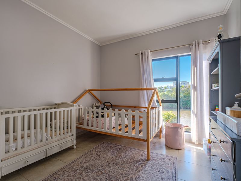 A bright bedroom featuring tiled flooring and a large window with natural light, currently utilized as a nursery.