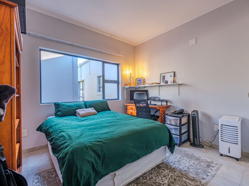A functional bedroom featuring tiled flooring, neutral wall finishes, and an aluminium-framed window providing natural light.