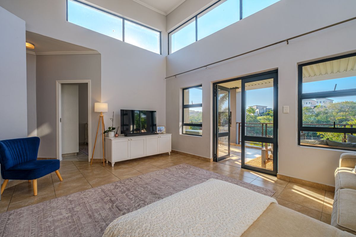 Spacious living room featuring high ceilings, clerestory windows for natural light, and direct access to a balcony through aluminium sliding doors.