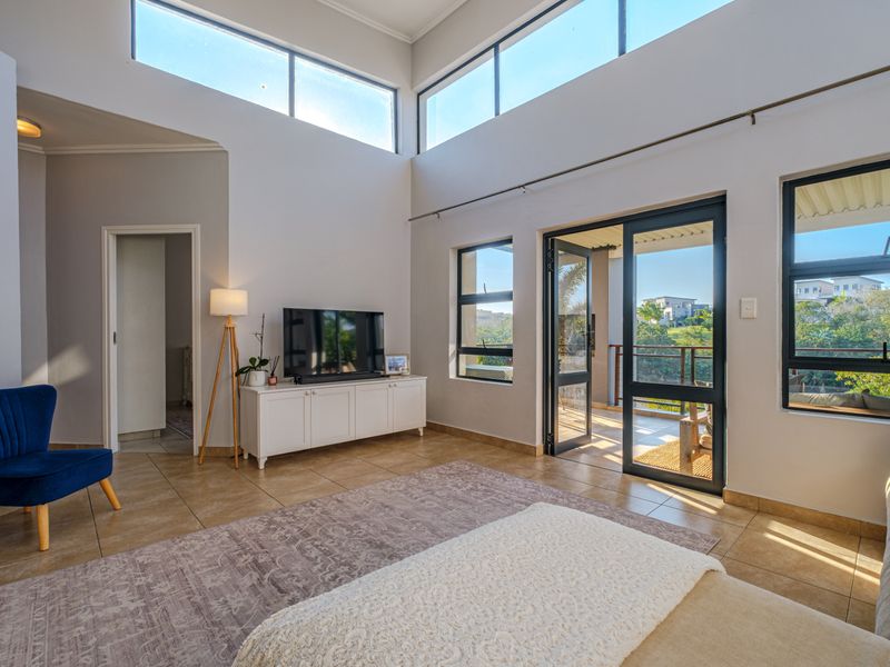 Spacious living room featuring high ceilings, clerestory windows for natural light, and direct access to a balcony through aluminium sliding doors.