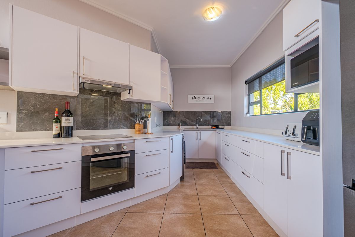 Modern kitchen featuring white cabinetry, stone countertops, built-in oven, electric hob, and a sleek stone splashback with tiled flooring.
