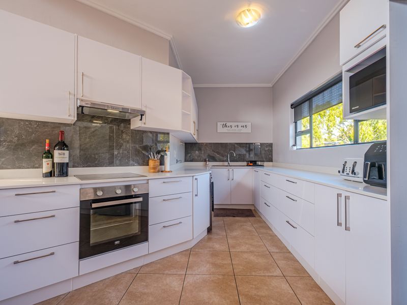 Modern kitchen featuring white cabinetry, stone countertops, built-in oven, electric hob, and a sleek stone splashback with tiled flooring.