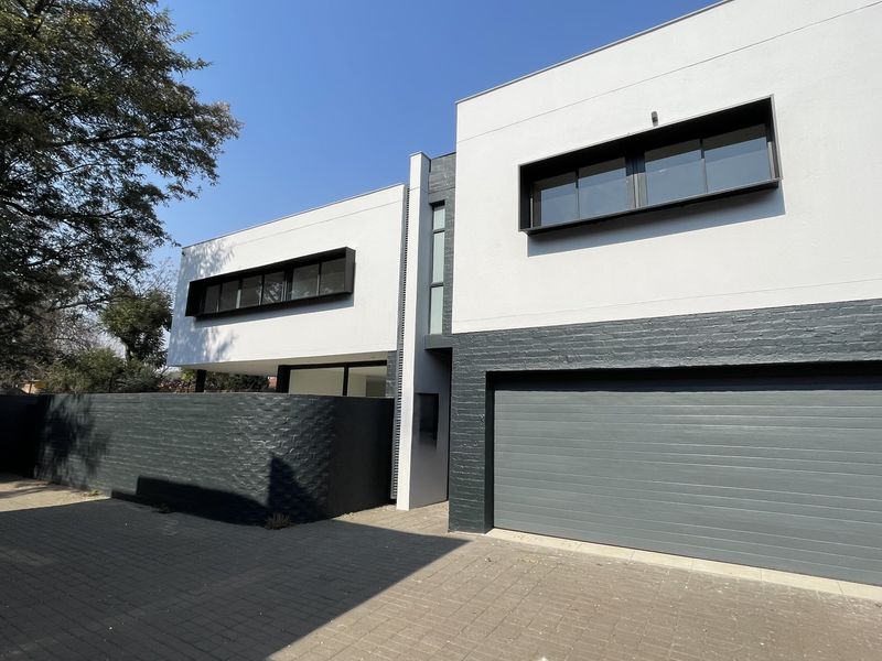Modern townhouse exterior featuring a clean white and dark grey facade, paved driveway, and integrated double garage.