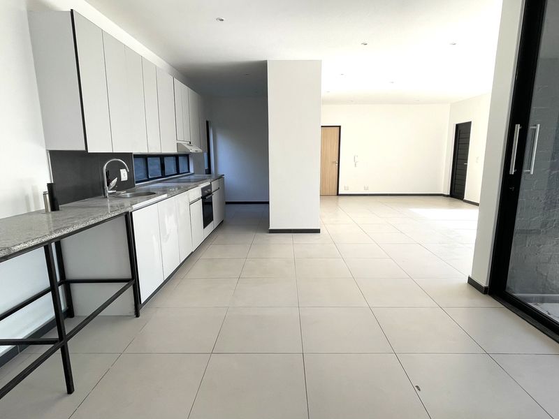 Spacious open-plan kitchen and living area featuring modern white cabinetry, granite countertops, tiled flooring, and large sliding glass doors leading to the exterior.