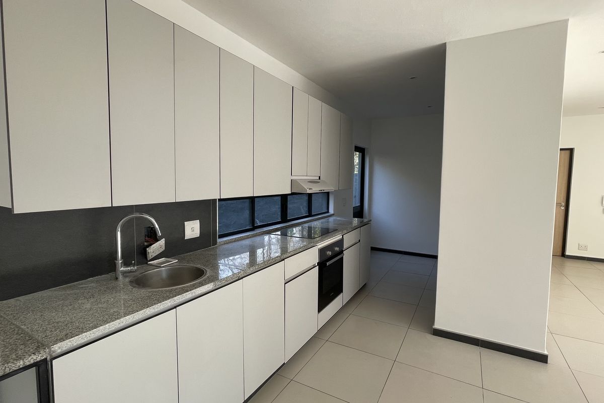 Modern kitchen featuring sleek light-grey cabinetry, granite countertops, integrated oven and hob, and tiled flooring in an open-plan layout.