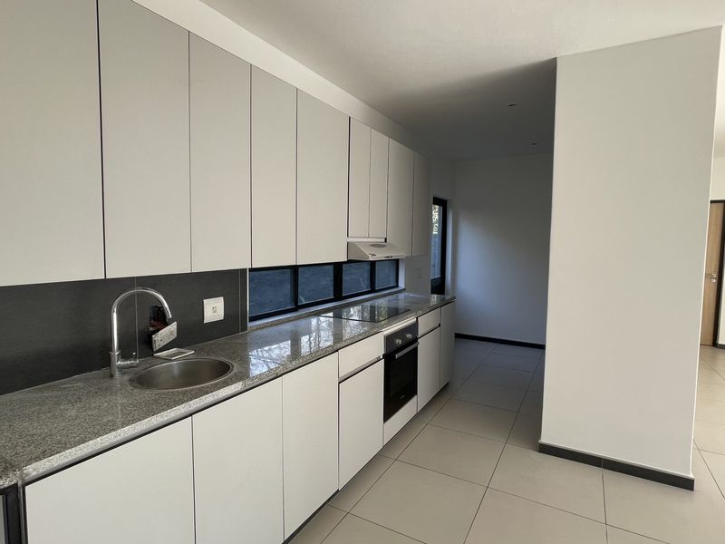 Modern kitchen featuring sleek light-grey cabinetry, granite countertops, integrated oven and hob, and tiled flooring in an open-plan layout.