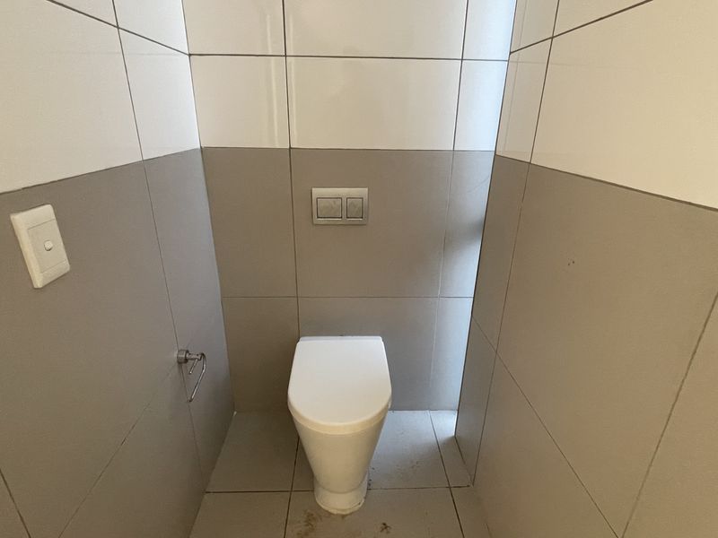 A compact guest bathroom featuring a modern wall-mounted toilet with a dual flush system and neutral two-tone tiled walls.