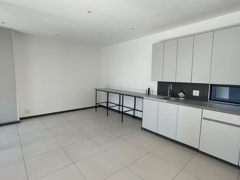 Modern kitchen featuring sleek grey cabinetry, stone countertops, built-in oven, and tiled flooring, with direct access to outdoor space via sliding glass doors.