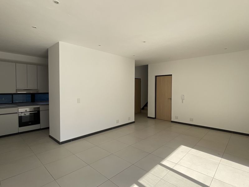 Spacious open-plan living area featuring modern kitchen cabinetry, integrated oven, neutral tiled flooring, and recessed lighting throughout.