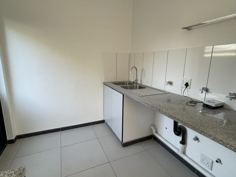 A functional laundry area featuring a stainless steel sink, granite countertop, tiled splashback, and dedicated plumbing connections for appliances.