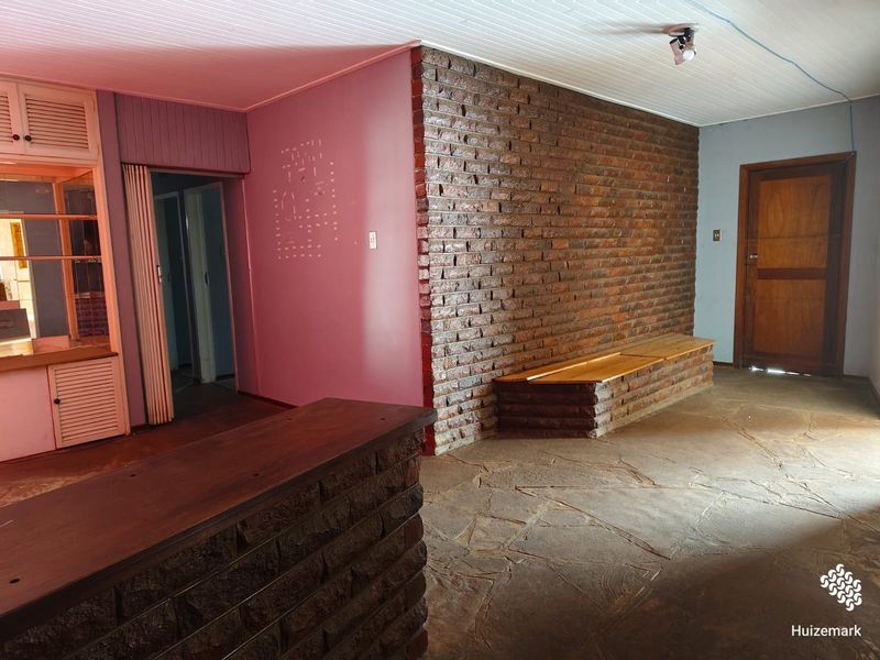 Spacious living area featuring a prominent exposed brick wall, built-in bench seating, and rustic flagstone flooring, offering a unique foundation for renovation.