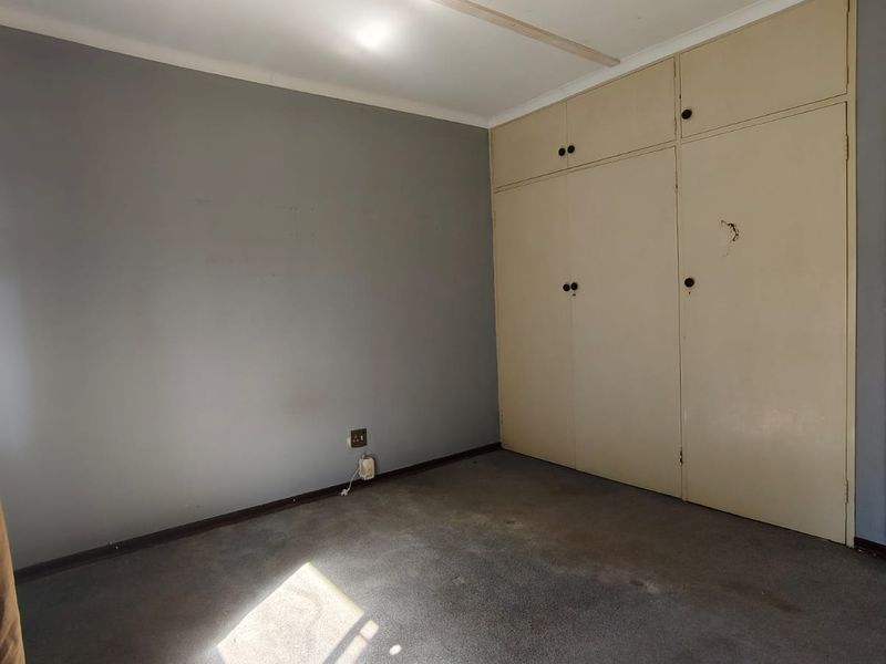An empty bedroom featuring built-in cupboards, grey wall paint, and carpet flooring, requiring cosmetic updates to improve its overall condition.