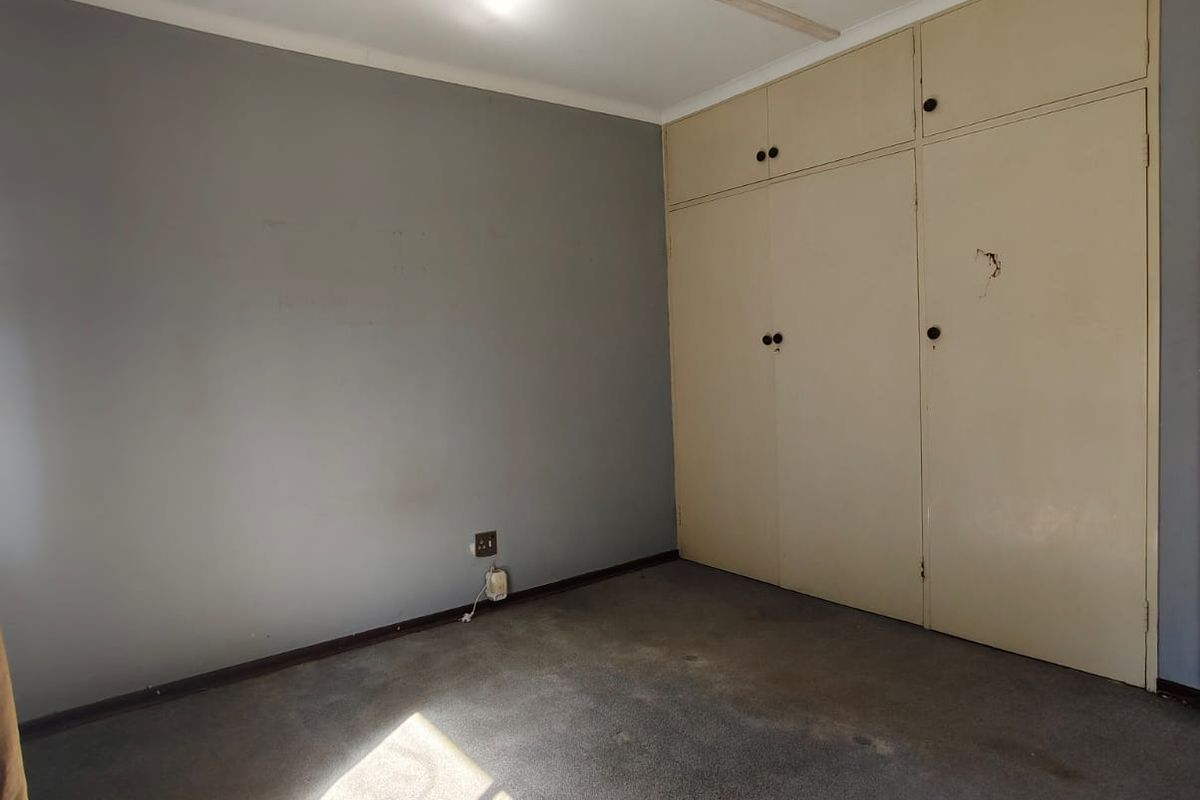 An empty bedroom featuring built-in cupboards, grey wall paint, and carpet flooring, requiring cosmetic updates to improve its overall condition.