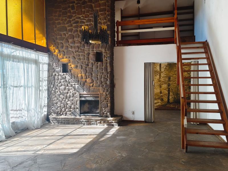 Spacious living room featuring a prominent stone fireplace, timber ceiling, flagstone flooring, and a timber staircase leading to a mezzanine level.